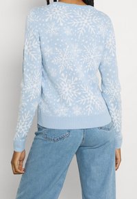 Helles blaues Sweatshirt mit weißen Schneeflockenmuster, geripptem Saum und Bündchen sowie einem klassischen Rundhalsausschnitt. Glatte Strickstruktur.