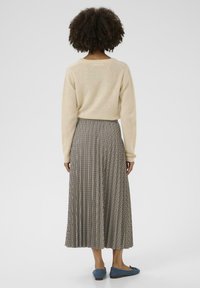 Cremefarbener Pullover mit langen Ärmeln, heller karierter Plissee-Rock in Schwarz und Beige, kombiniert mit blauen Ballerinas. Rückansicht.