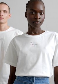 Tricou alb din bumbac cu mâneci scurte și decolteu în formă rotundă, având brodat cu fir multicolor cuvântul "Love" pe piept.