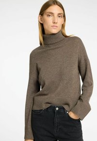 Brauner Rollkragenpullover mit gerippter Textur und langen Ärmeln, kombiniert mit hoch sitzenden schwarzen Jeans. Lässige, moderne Passform.