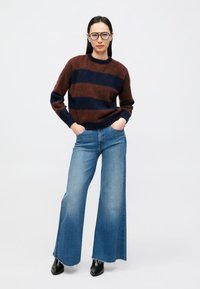 Pulover cu dungi maro și bleumarin, cu guler rotund, asortat cu blugi evazați albaștri. Ținuta este completată cu ghete negre până la gleznă.