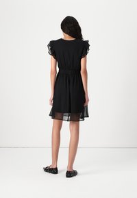 Black dress with ruffle sleeves, elastic waist, and sheer overlay, featuring a fitted bodice and flared skirt, worn with black flat shoes.