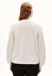 White knitted sweater with a ribbed texture, dropped shoulders, and a relaxed fit, featuring long sleeves and a straight hem.