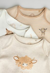 Tre babymössor: en krämfärgad med en koillustration, en beige randig och en ljusbrun med ett tecknat kornötsmönster. Mjukt tyg, rund hals.