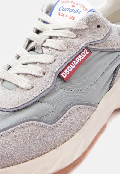 Baskets gris clair et beige avec des lacets blancs, étiquette logo DSQUARED2 rouge, et texte "Canada Dean & Dan" sur la languette.