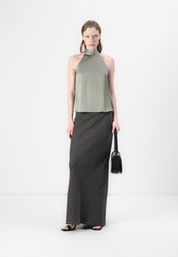 Olivenfarget halterneck-top kombinert med et langt svart skjørt med hvite diagonale striper. Hun har med seg en liten svart veske og har på seg sandaler med åpen tå.