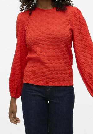 Czerwony, teksturowany longsleeve z okrągłym dekoltem i balonowymi rękawami, zestawiony z ciemnoniebieskimi dżinsami, prezentujący luźny krój.