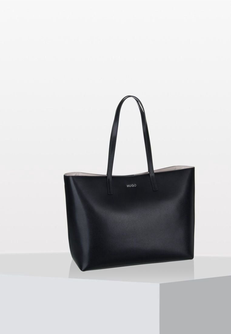 Borsa tote in pelle nera con due manici lunghi, lati piatti e un marchio sobrio al centro. Texture liscia e design minimalista.