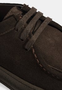 Chaussures en daim marron foncé avec un bout arrondi, ornées de lacets texturés, de coutures contrastantes et d'une semelle en caoutchouc lisse.
