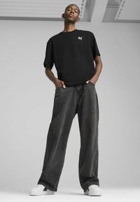 T-shirt nera in cotone con piccolo logo ricamato, abbinata a jeans in denim scuri e larghi e scarpe da ginnastica bianche.