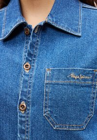 Πουκάμισο από τζιν σε σκούρο μπλε με γιακά, καφέ κουμπιά και τσέπη στο στήθος με χρυσή κεντημένη επωνυμία "Pepe Jeans".