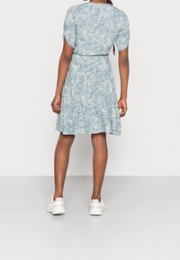 Ljusblå klänning med vitt blommönster, korta ärmar, åtsmitande midja och vida kjol, kombinerad med vita sneakers.