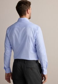Cămașă button-up albastru deschis, cu mânecă lungă, având un guler clasic și un model discret în carouri, asortată cu pantaloni gri și un buzunar posterior cu buton.