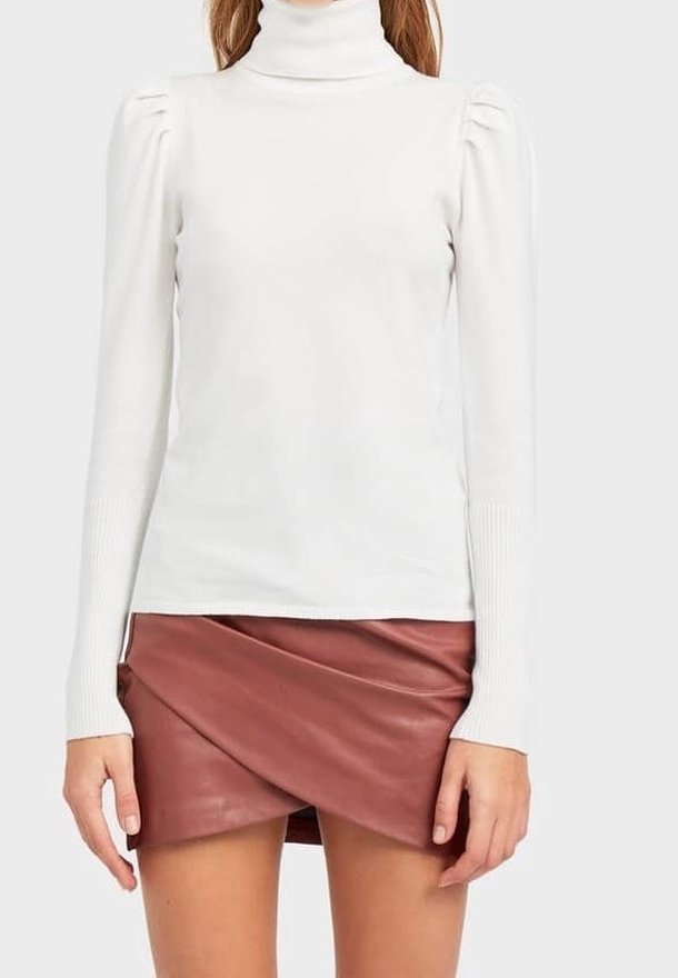 Pull à col roulé blanc avec détails bouffants sur les épaules et poignets côtelés, associé à une mini-jupe portefeuille en cuir bordeaux.