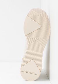 Beige podeševka boty s texturovanou gumou, geometrickými vzory a hladkým povrchem. Název značky "Michael Kors" vyražený poblíž paty.