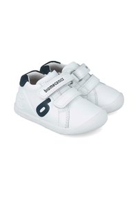 Zapatos de cuero blanco con acentos en azul marino, presentan dos correas de Velcro, punta redonda y suela de goma texturizada, marcados con "biomecánica."