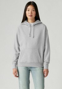 Felpa grigia in cotone con tasca frontale, cappuccio con lacci e polsini a costine. Abbinata a jeans chiari strappati.