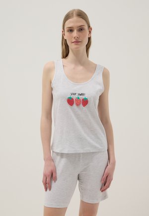 Mujer joven con conjunto gris claro sin mangas y pantalones cortos, con tres fresas y el texto "STAY SWEET" en la parte delantera de la camiseta.