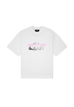 Femme portant un t-shirt blanc ample avec un texte pastel « HIDDEN GEM » et un motif d’huître, pantalon large crème et chaussures noires, debout sur un fond gris.