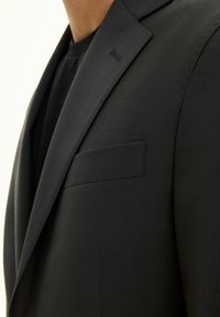 Blazer nero su misura con collo a punta, taschino sul petto e texture liscia. La vista in primo piano mette in evidenza i dettagli della cucitura pulita.