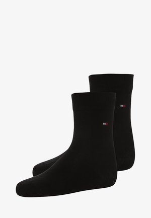 Calcetines negros hasta el tobillo hechos de una tela suave con un diseño acanalado. Presentan un pequeño logo en rojo, blanco y azul en el lateral.