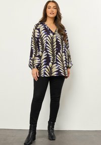Blusa a maniche lunghe e scollatura a V di colore viola scuro con motivi di foglie gialle e bianche, abbinata a jeans skinny neri e stivaletti alla caviglia.