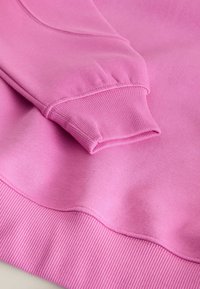 Hanorac roz cu manșete și tiv din material ribbat, realizat dintr-un material moale, având o textură netedă și fără modele vizibile sau detalii metalice.