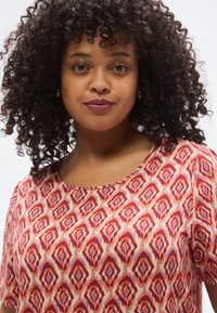 Κοντομάνικη μπλούζα από ελαφρύ υφαντό ύφασμα με κόκκινο και κρεμ γεωμετρικό σχέδιο και διακριτικές μωβ λεπτομέρειες. Στρογγυλή λαιμόκοψη.