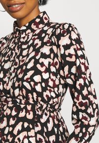 Leopardmönstrad klänning med svart botten, med rosa och vita fläckar, krage och långa puffärmar. Knuten midja för accent.