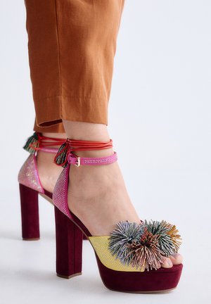 Sandalias de plataforma con tacón alto, adornadas con piedras multicolores, pompones en los dedos, tiras rosas en el tobillo y tacones de ante burdeos.