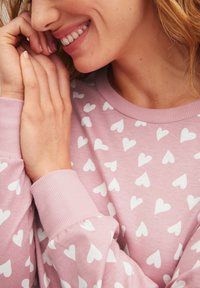 Lichtroze sweatshirt gemaakt van zachte stof, met witte hartpatronen. Ribgebreide manchetten en halslijn voegen textuur toe aan het ontwerp.