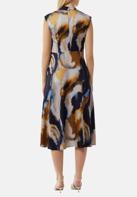Ärmelloses Kleid mit floralem Muster und hohem Kragen in Blau-, Braun- und Cremetönen. Verfügt über einen Knopfverschluss auf der Rückseite. Midi-Länge.