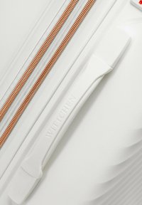 Weißer Koffer mit einer strukturierten Oberfläche, ausgestattet mit einem kupferfarbenen Reißverschluss und einem weißen Griff, der mit "Wittchen"prägung versehen ist.