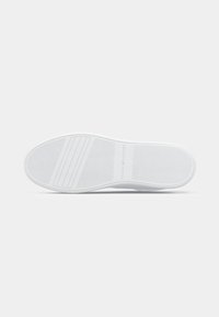 Die Sohle des weißen Sneakers mit strukturiertem Grip und "Tommy Hilfiger"-Prägung in der Mitte, flach auf einem weißen Hintergrund dargestellt.