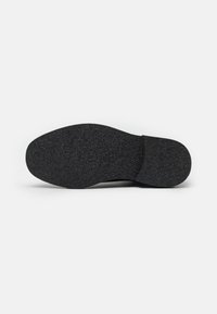 Suela de zapato negra hecha de goma texturizada, con un perfil plano y punta redondeada. Diseñada para ofrecer tracción con un borde liso.