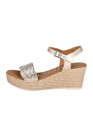 Sandalia de cuña con suela plataforma trenzada beige, tira frontal metálica trenzada y correa ajustable en el tobillo con hebilla.