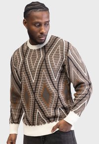 Brown patterned sweater with diamond shapes in beige, white, and rust. Ribbed white cuffs and hem. Made from textured knit fabric.