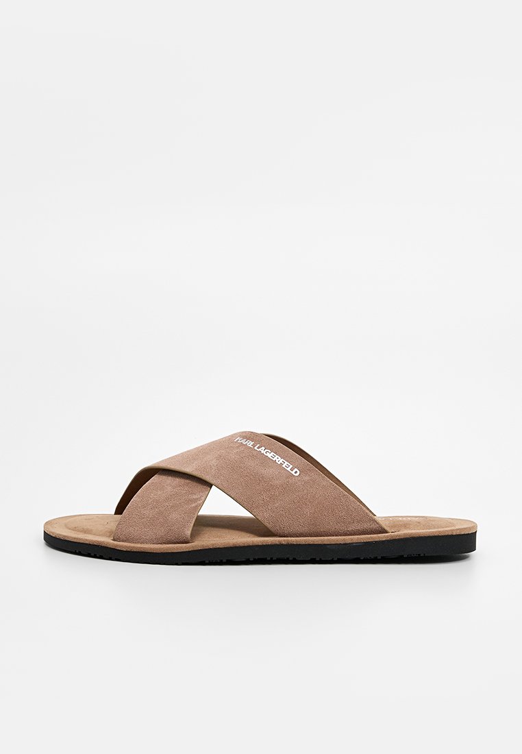 Braune Wildleder-Sandale mit überkreuztem Riemendesign, flacher schwarzer Gummisohle und weißem Logo der Marke auf dem oberen Riemen.