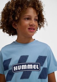 Lyseblå bomulds T-shirt med marineblå teksturerede skrå striber og "HUMMEL" logo i et afrundet rektangulært design. Korte ærmer.