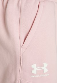Ljusa rosa joggingbyxor i mjukt tyg med sidoficka och en vit Under Armour-logga på nedre benet. Mjuk textur, avslappnad design.