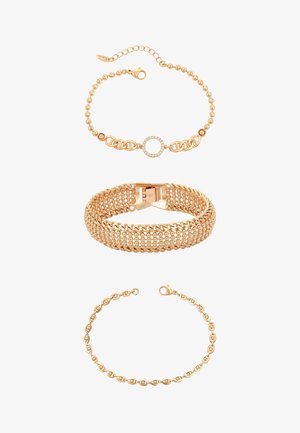 Trzy złote bransoletki: górna z koralikowym łańcuszkiem i diamentowym kółkiem, środkowa szeroka pleciona zapięta klamrą, dolna delikatny łańcuszek z zapięciem typu karabińczyk.