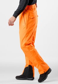 Oranje waterdichte broek met verstelbare taille, grote zakken en zwarte accenten aan de boorden. Ontworpen voor buitenactiviteiten.