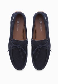 Navyblaue Wildleder Slipper mit runder Zehenform, ausgestattet mit einer Schleifendetail, kontrastierendem braunem Innenfutter und sichtbaren Nähten, geeignet für die Freizeit.