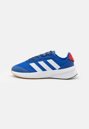 Niebieskie buty sportowe z białymi paskami, teksturowana cholewka, szare sznurówki, czerwony akcent przy pięcie i biała, amortyzowana podeszwa.