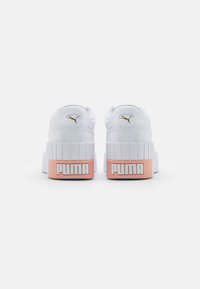 Baskets blanches avec un matériau texturé, présentant une semelle épaisse et striée. Accentuées par un logo Puma doré et un onglet au talon rose.