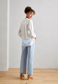 Sac bandoulière bleu clair avec motif matelassé et ferrures dorées ; porté sur une chemise en lin blanche et associé à un jean large bleu clair.