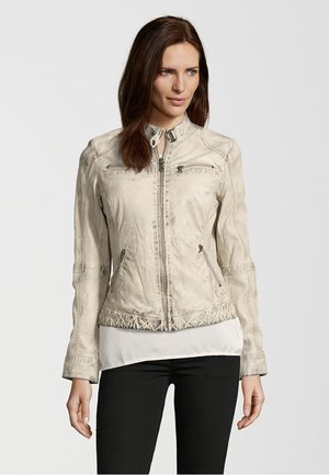 Beige Lederjacke mit tailliertem Schnitt, Reißverschluss vorne, dekorativen Nähten und zwei Reißverschlusstaschen, getragen über einem weißen Oberteil.