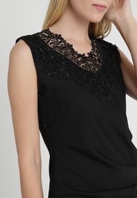 Haut noir sans manches avec un col en dentelle noire détaillé. Le tissu a une texture lisse et une coupe ajustée.