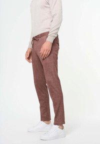 Pantalones de lino marrones con cintura ajustable, corte entallado y bolsillos delanteros, combinados con zapatillas blancas y un suéter ligero.