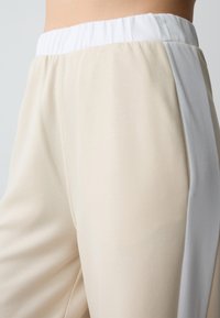 Beige en lichtgrijze trainingsbroek met een elastische tailleband en een gladde textuur. De zijnaden versterken het slanke ontwerp.